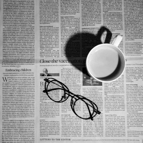 a cup of coffee and a pair of glasses on a newspaper